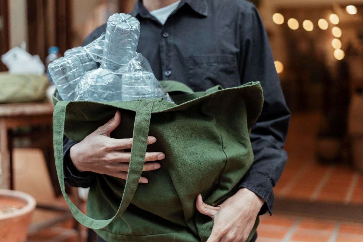 A person holds a reusable bag full of empty plastic bottles to return through the Pant system.