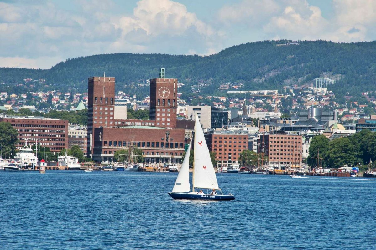 View of Oslo City Hall from the sea, with a sailboat in the foreground.