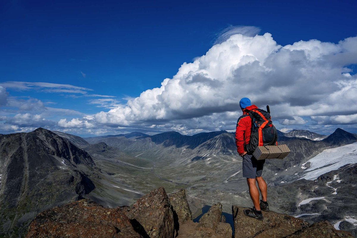 A hiker with a backpack stands on a summit overlooking the mountains.