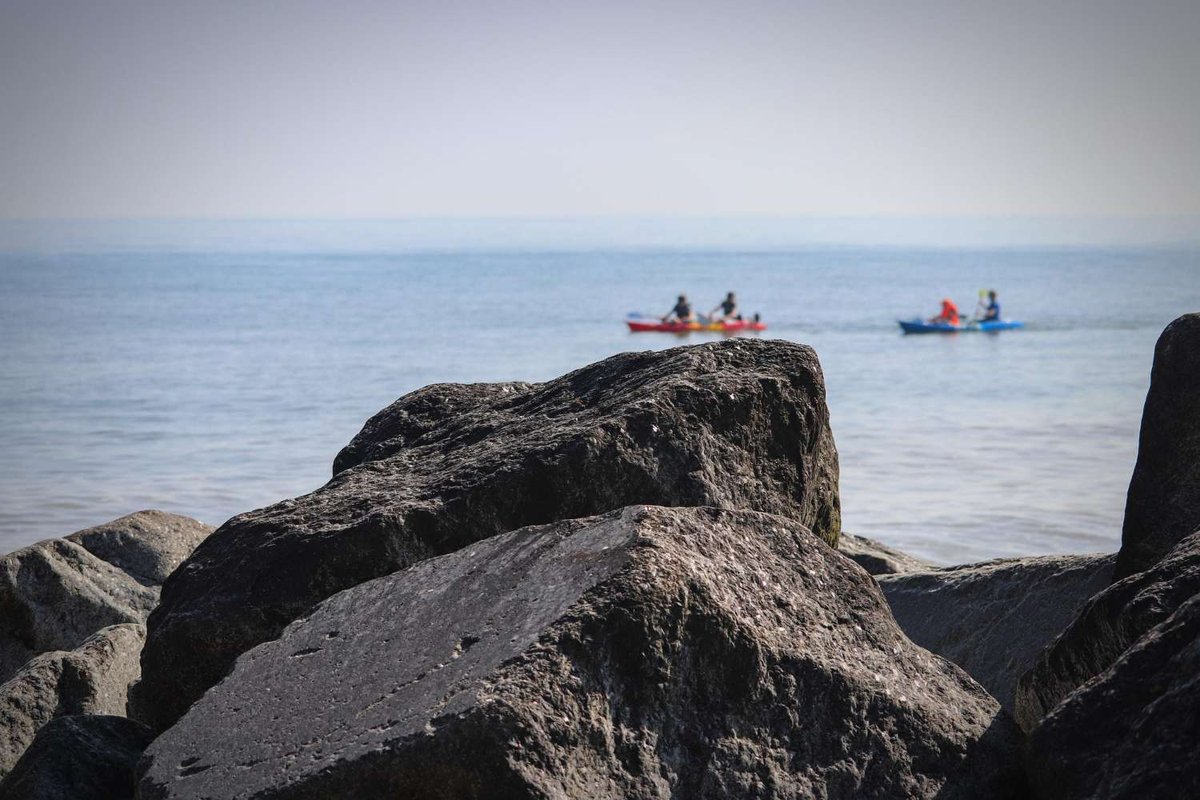 People kayak along the sea near a rocky shoreline.