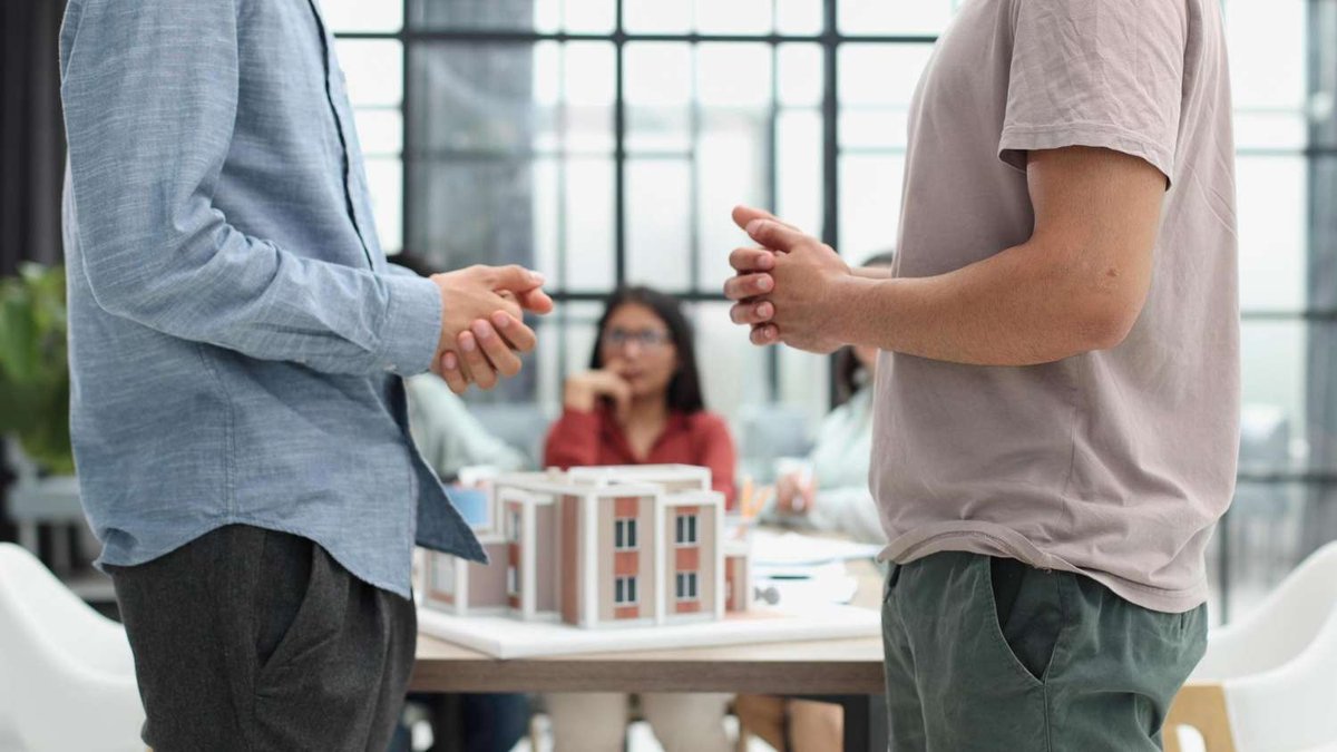 Two people are discussing rental terms in front of a residential building model.