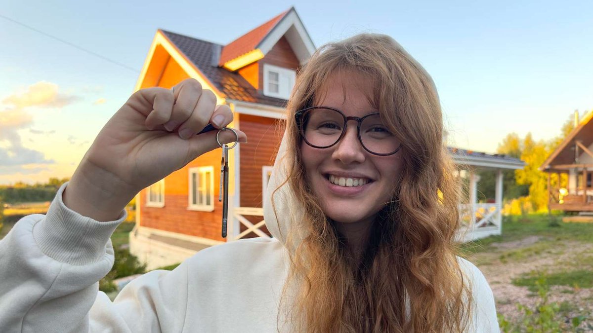 A young woman holding keys in front of a private house in the countryside.