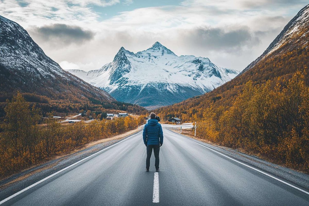 A traveler stands in the middle of the road leading to a snowy peak.