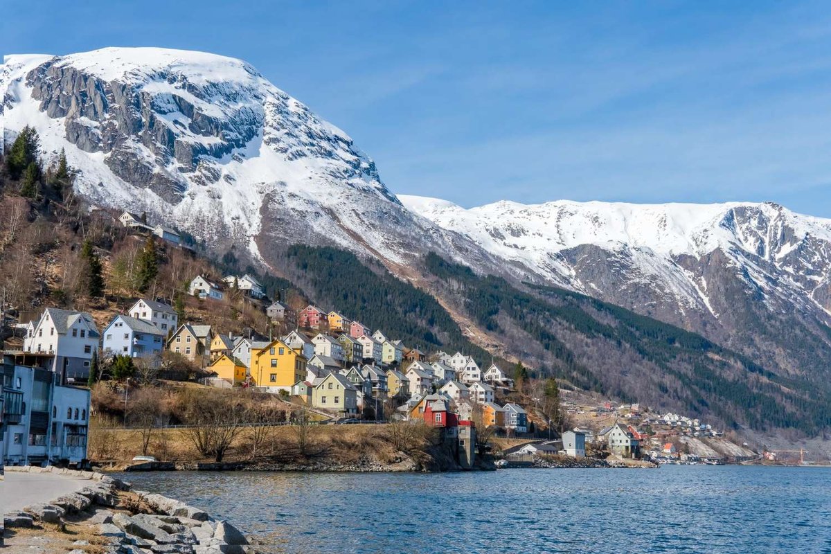 A small town with colorful houses lies by the fjord and snowy mountains.