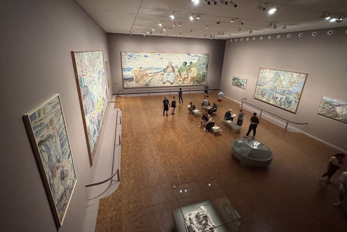 A gallery hall at the MUNCH Museum in Oslo featuring large-scale paintings by Edvard Munch and visitors exploring the artist&#x27;s works.