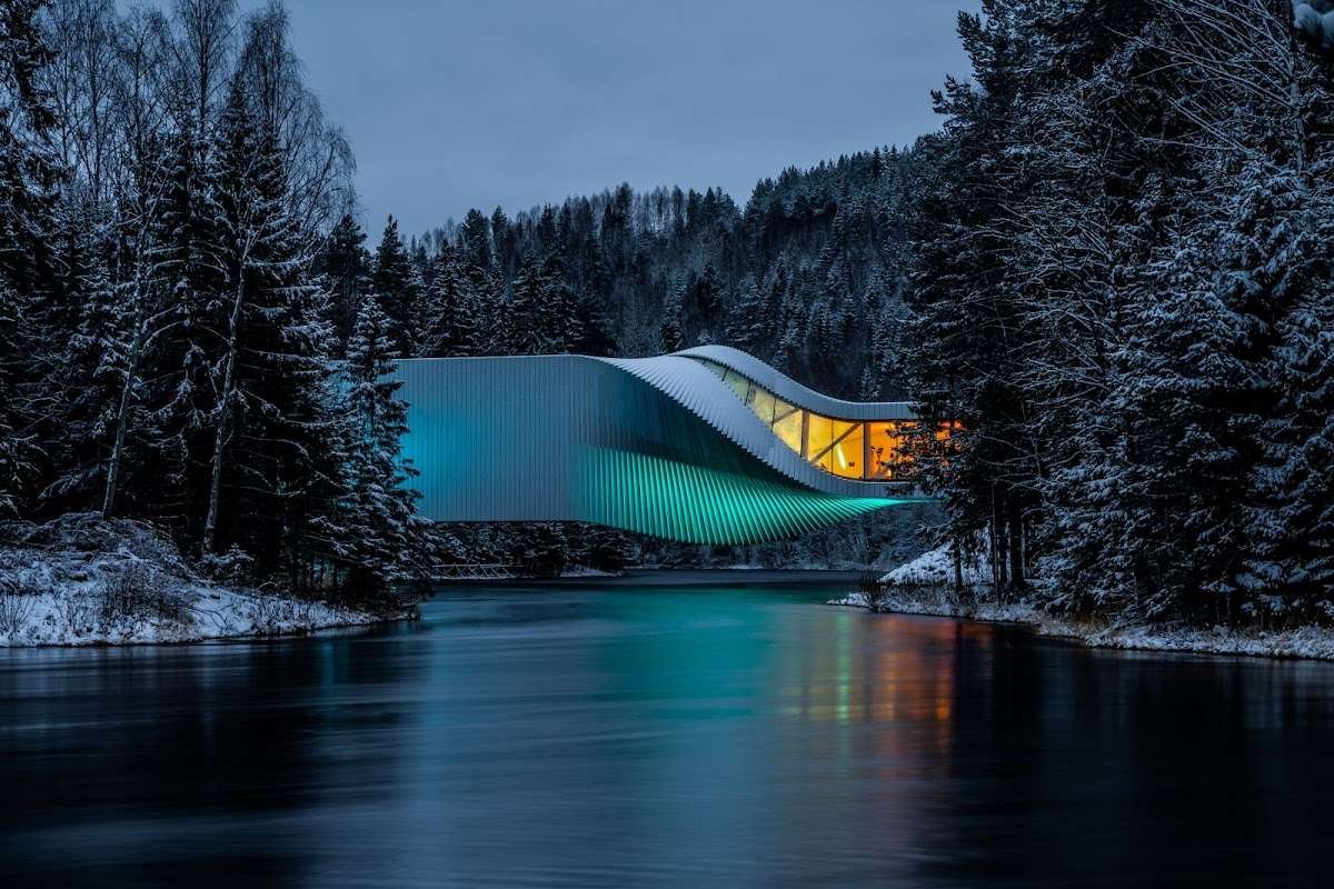 The Twist gallery in Kistefos, Norway, captured in a winter landscape with colorful lighting and river reflections.