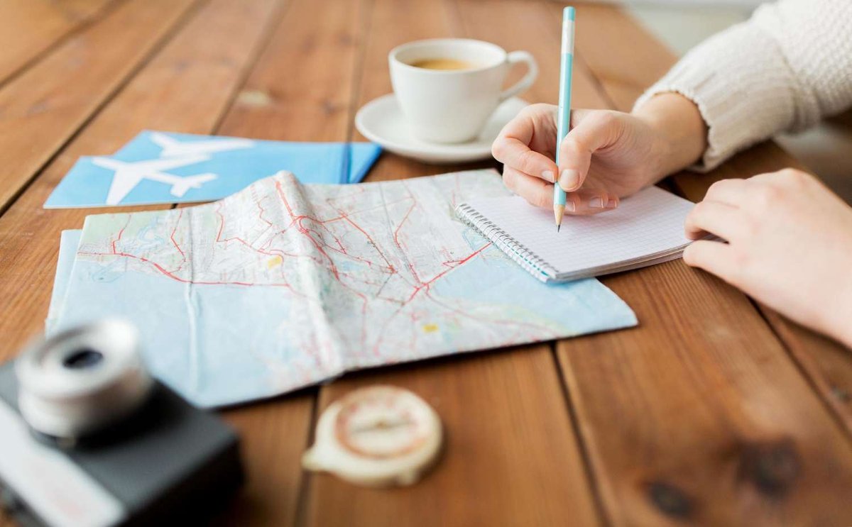 A person writes travel notes using a map and a notebook.