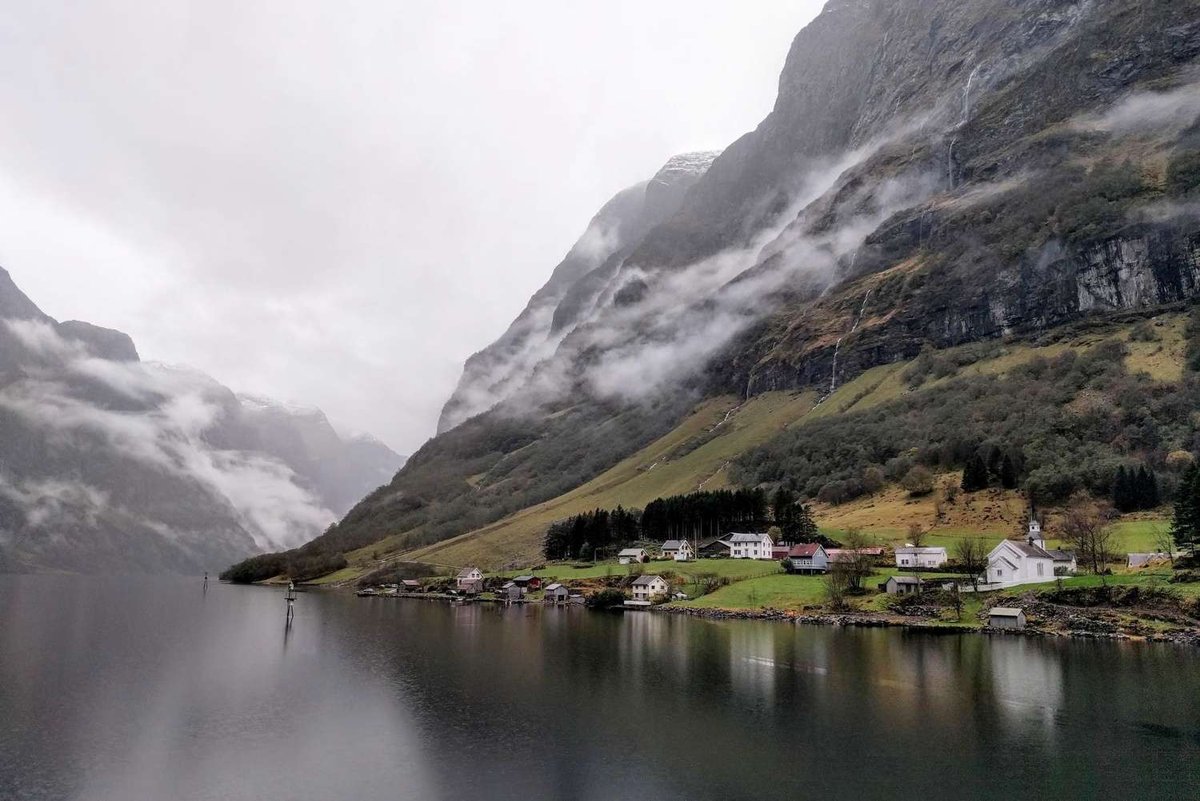A small Norwegian village lies at the foot of misty mountains by the fjord.
