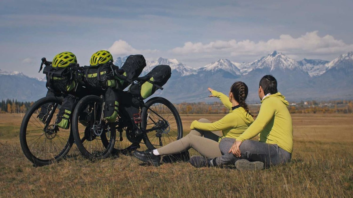 Two cyclists are resting with a view of snow-covered mountains during their journey.