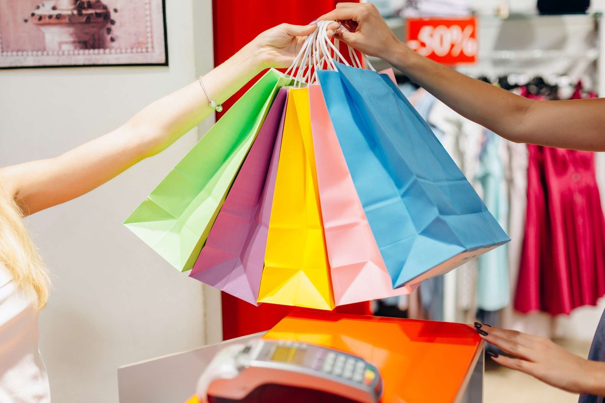Close-up of colorful shopping bags being handed over at the checkout counter during a sale. Symbol of retail shopping and fashion deals.