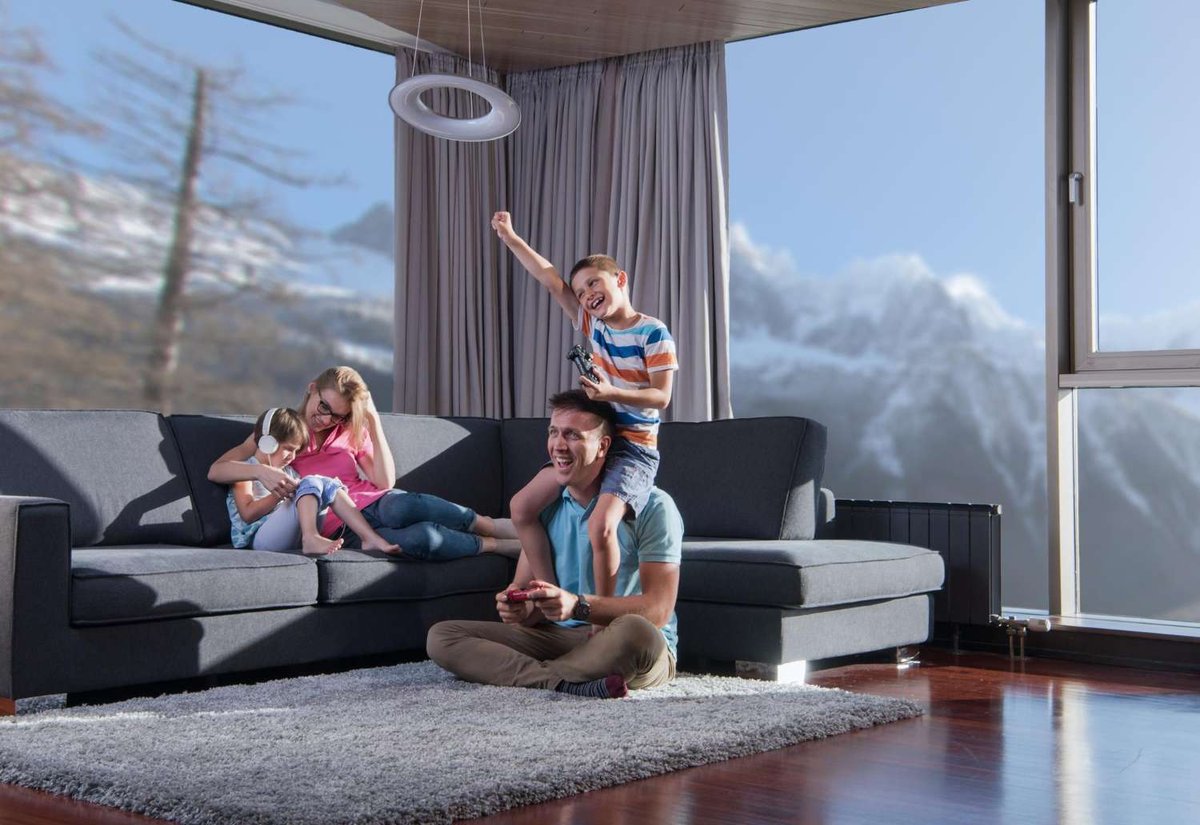 A family enjoys cozy time indoors with a panoramic mountain view from a modern apartment in Norway.