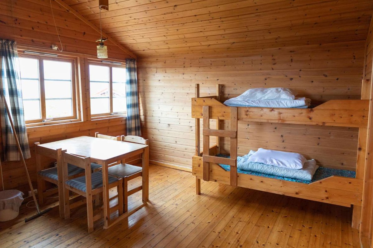 A simple wooden room with a bunk bed and table in a Norwegian hostel.