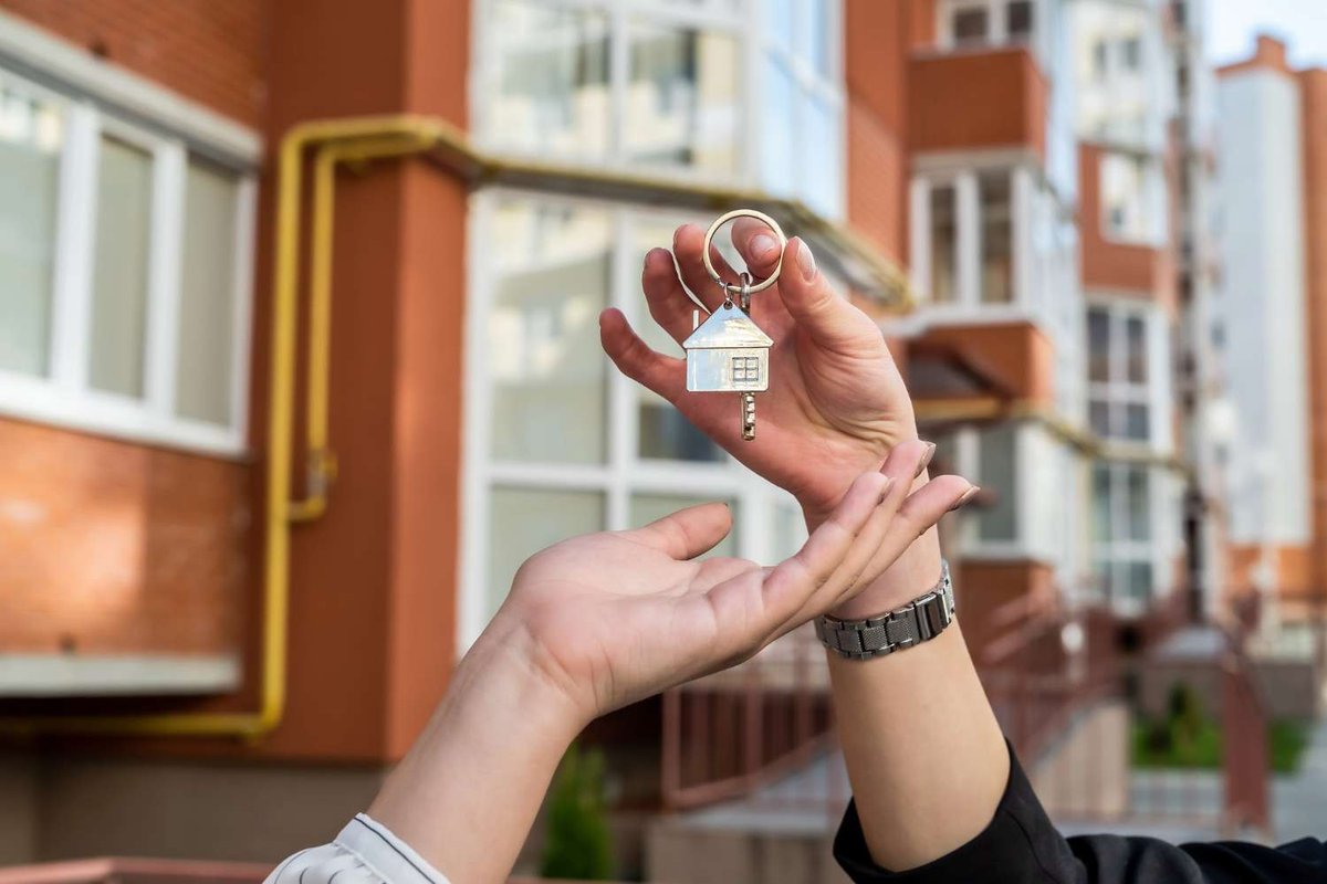 A person hands over apartment keys in front of a residential building.
