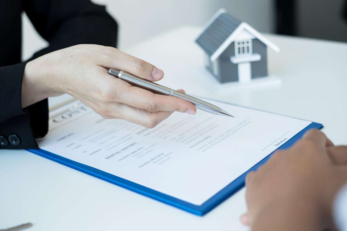 A person points with a pen at a housing rental agreement on the table.
