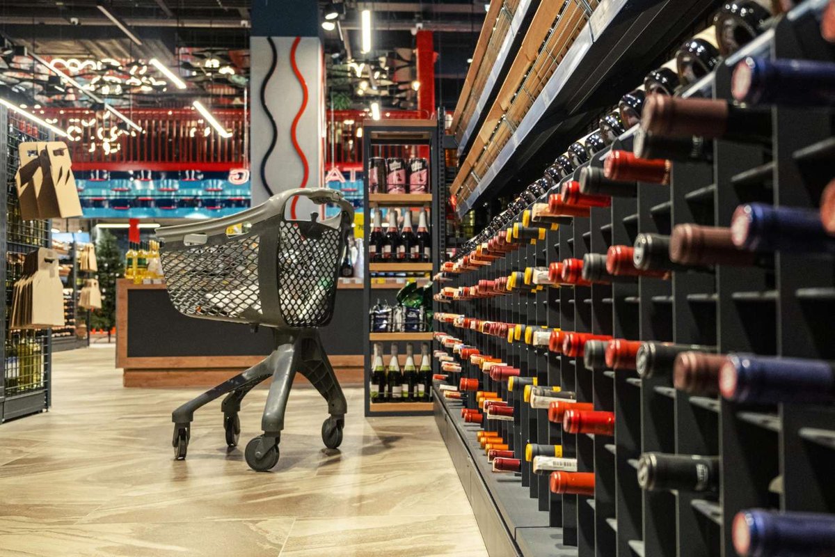 Wine section in a liquor store with a shopping cart and neatly arranged bottles. Ideal visual for articles about wine shopping or alcohol retail.